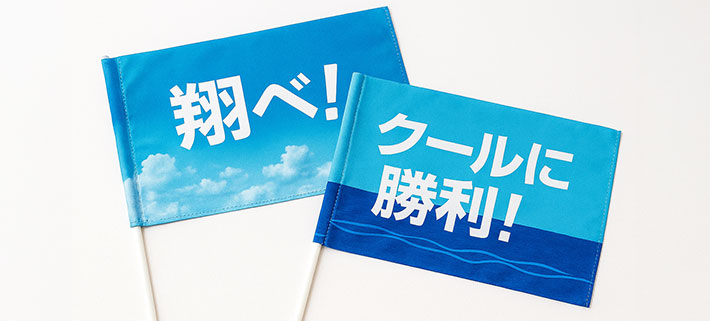 「翔べ！」と名入れ印刷された、空をモチーフにした青色の応援旗と「クールに勝利！」と名入れ印刷された海をモチーフにした応援旗のイメージ画像