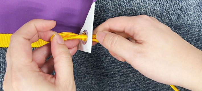 紐を二つ折りにして、紐の折り目をハトメに通している画像