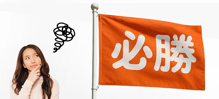 オレンジ色の生地に白の太字で「必勝」という文言が名入れ印刷された、オリジナル応援旗の横で製作する際の注意点について考えている人のイメージ画像