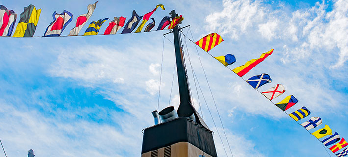 船の上部に掲げられた複数の国際信号旗が青空の下、はためいているイメージ画像