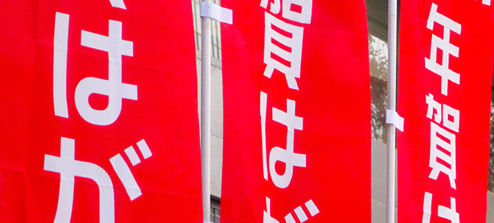 年賀はがきをPRするために製作された、赤色の旗広告・フラッグ広告がはためいている画像