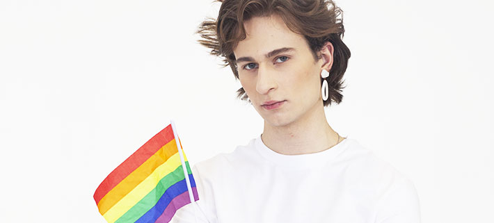 LGBTQ+の当事者がレインボーフラッグの手旗を持ってコチラを見つめている写真