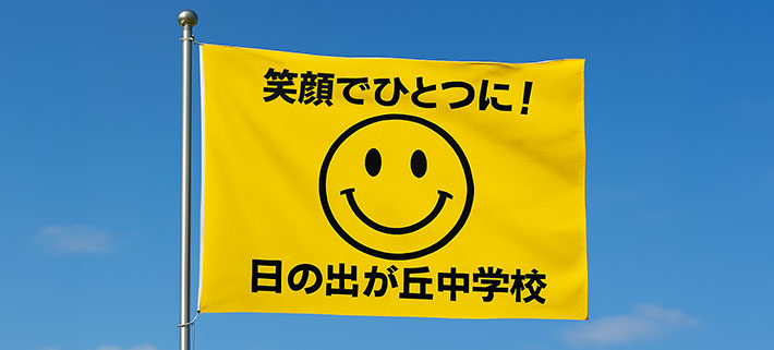 黄色の生地の中心部分にスマイルマーク、スマイルマークの上部には「笑顔でひとつに！」という文言、ロゴマークの下部には「日の出が丘中学校」という文言が、黒色で名入れ印刷された、オリジナル応援旗のイメージ画像